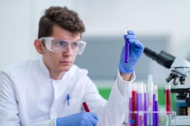 young student with protective glasses making chemistry experiment in bright laboratory,education and medicine concept