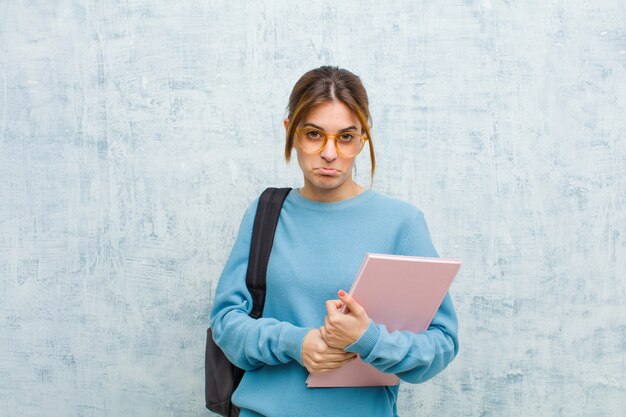 Young student woman feeling sad and whiney with an unhappy look, crying with a negative and frustrated attitude against grunge wall