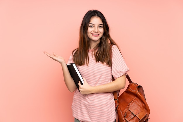 Giovane donna dello studente che va all'università sopra la parete rosa che tiene immaginario dello spazio in bianco sul palmo