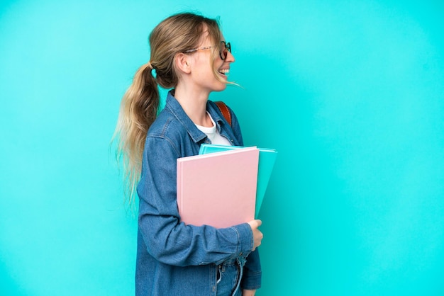 Young student woman isolated on blue background laughing in lateral position