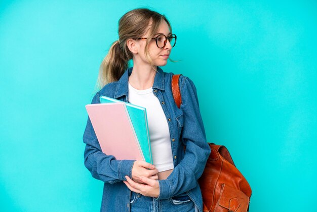 Young student woman isolated on blue background looking to the side