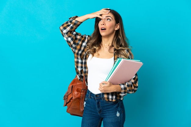 Young student woman isolated on blue wall doing surprise gesture while looking to the side