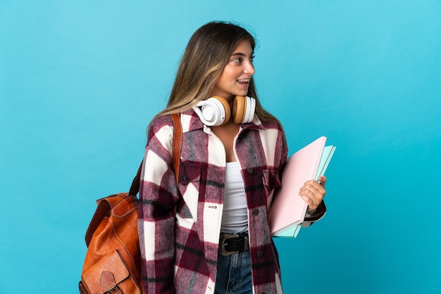 Young student woman isolated on blue wall looking side