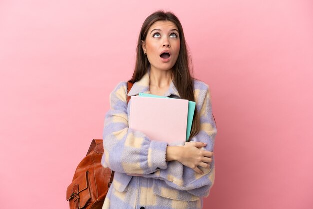 Young student woman isolated on pink background looking up and with surprised expression