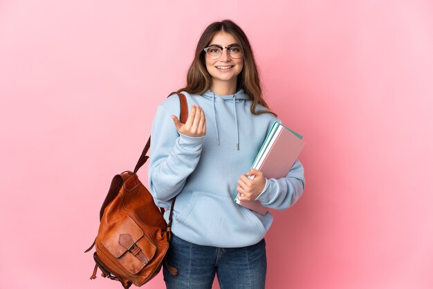 Young student woman isolated on pink inviting to come with hand. Happy that you came