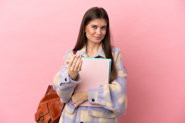 ピンクの壁に孤立した若い学生女性が手で来るように誘う。あなたが来て幸せ