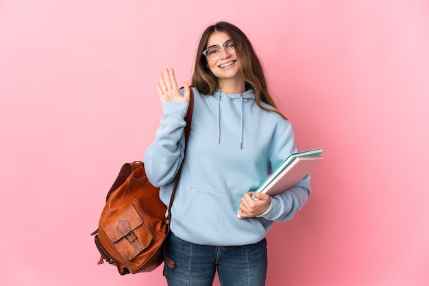 Young student woman isolated on pink wall saluting with hand with happy expression