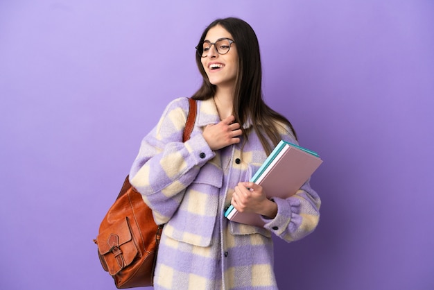 Молодая студентка женщина изолирована на фиолетовом фоне, глядя вверх, улыбаясь