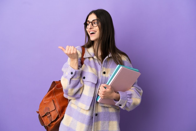 Young student woman isolated on purple background pointing to the side to present a product