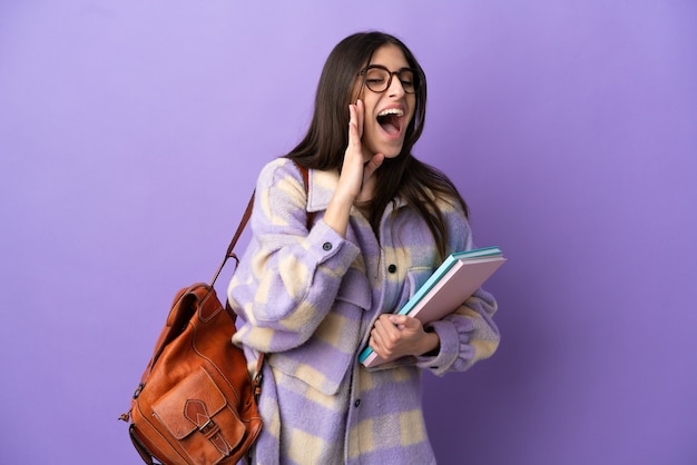 Young student woman isolated on purple background shouting with mouth wide open to the side