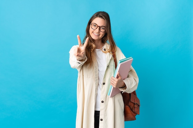 笑顔と勝利のサインを示す孤立した壁の上の若い学生女性