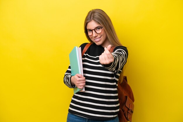 Young student woman isolated on yellow background background making money gesture
