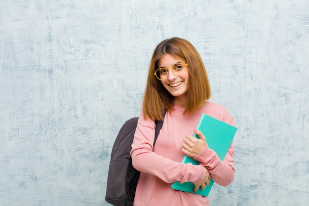 Young student woman laughing happily with arms crossed, with a relaxed, positive and satisfied pose against grunge wall 