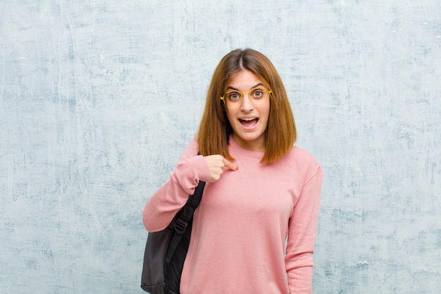 Young student woman looking happy, proud and surprised, cheerfully pointing to self, feeling confident and lofty