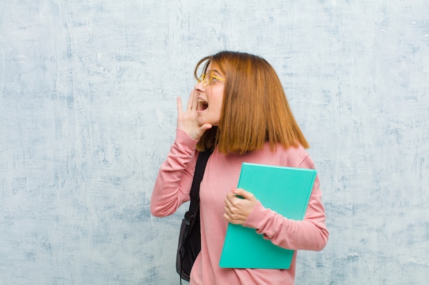 Young student woman profile view, looking happy and excited, shouting and calling to copy space on the side against grunge wall background