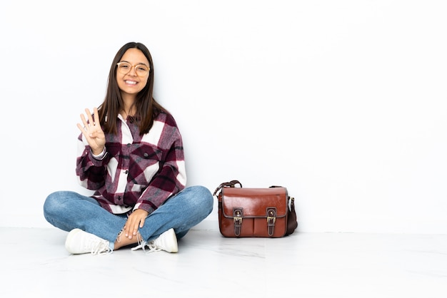 Young student woman sitting on the floor happy and counting four with fingers