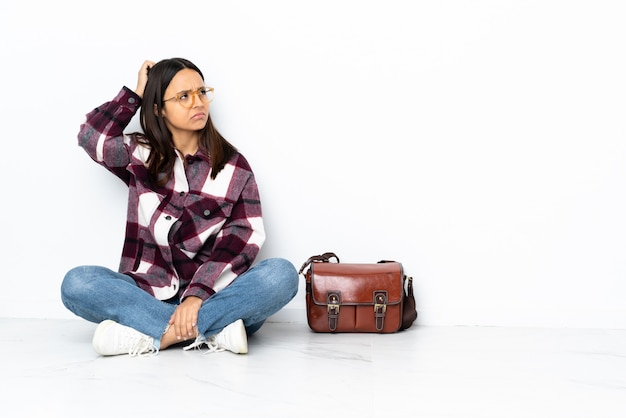 Young student woman sitting on the floor having doubts while scratching head