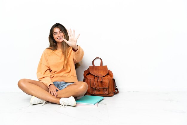 Young student woman sitting on the floor with a laptop isolated on white background counting five with fingers