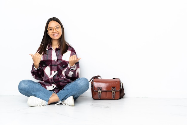 親指を立てるジェスチャーと笑顔で床に座っている若い学生女性