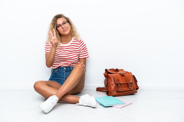 Young student woman sitting one the floor happy and counting three with fingers