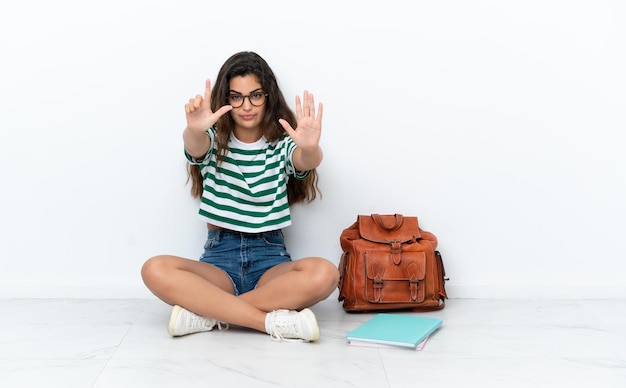 Young student woman sitting one the floor isolated on white background counting seven with fingers