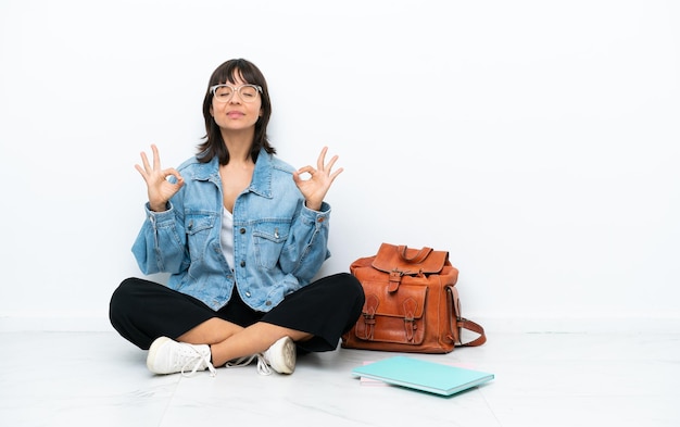 Young student woman sitting one the floor isolated on white background in zen pose