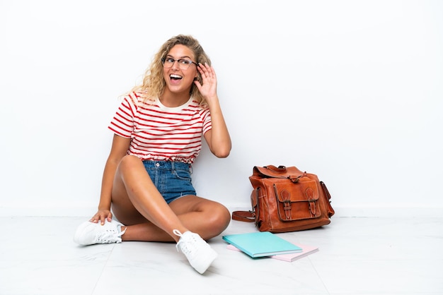 Young student woman sitting one the floor listening to something by putting hand on the ear