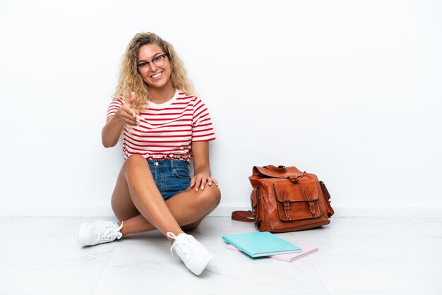 Young student woman sitting one the floor shaking hands for closing a good deal