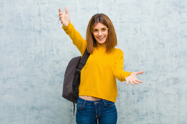 Young student woman smiling cheerfully giving a warm, friendly, loving welcome hug, feeling happy and adorable  grunge wall 