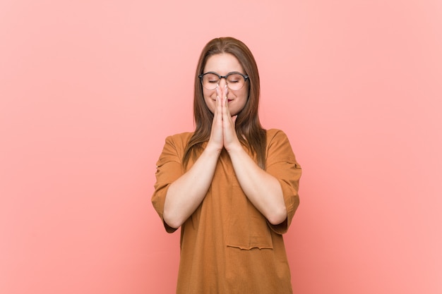 Young student woman wearing eyeglasses holding hands in pray near mouth, feels confident.