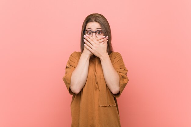 Young student woman wearing eyeglasses shocked covering mouth with hands