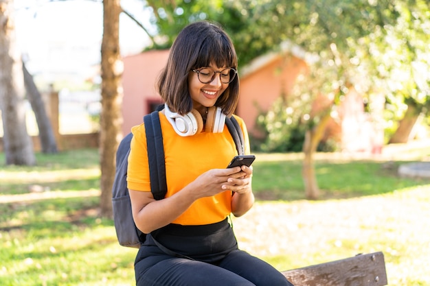 휴대 전화를 사용하여 공원에서 승리하는 젊은 학생 여성