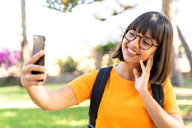 若い学生の女性が携帯電話を使って公園に勝つ