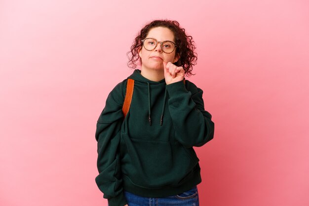 Young student woman with Down syndrome isolated on pink background with fingers on lips keeping a secret.