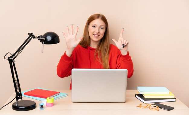 Young student woman in a workplace with a laptop counting seven with fingers