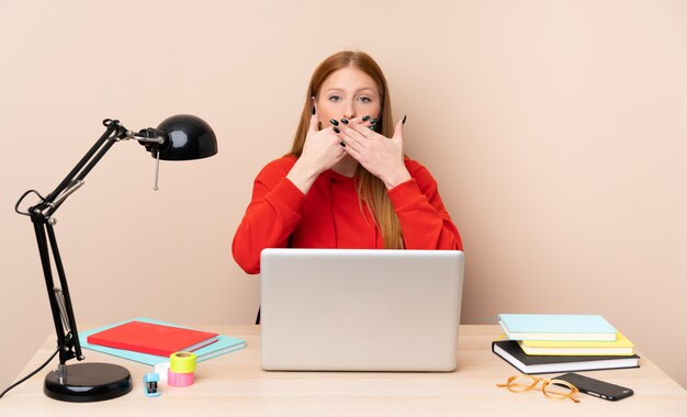 Молодой студент женщина на рабочем месте с ноутбуком, охватывающий рот руками