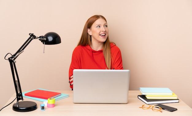 Giovane donna dello studente in un posto di lavoro con un computer portatile felice e sorridente