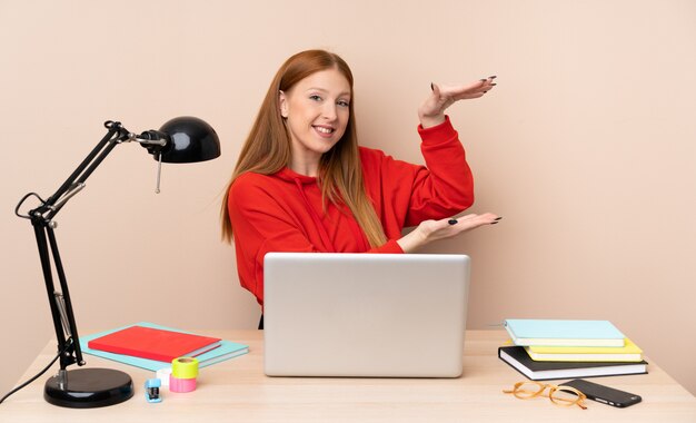 Young student woman in a workplace with a laptop holding something