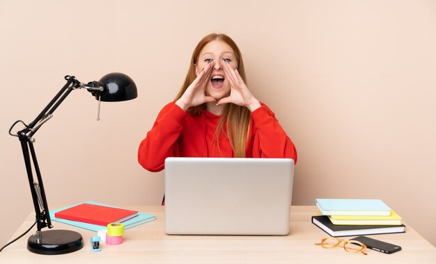 Young student woman in a workplace with a laptop shouting and announcing something