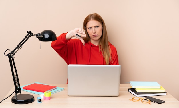 Young student woman in a workplace with a laptop showing thumb down with negative expression