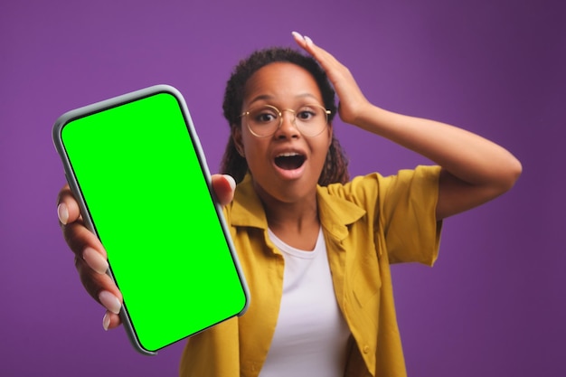 Young stunned african american woman clutching head demonstrates screen of phone