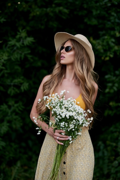 Giovane splendida ragazza in un abito estivo e con fiori bianchi nelle sue mani nella foresta