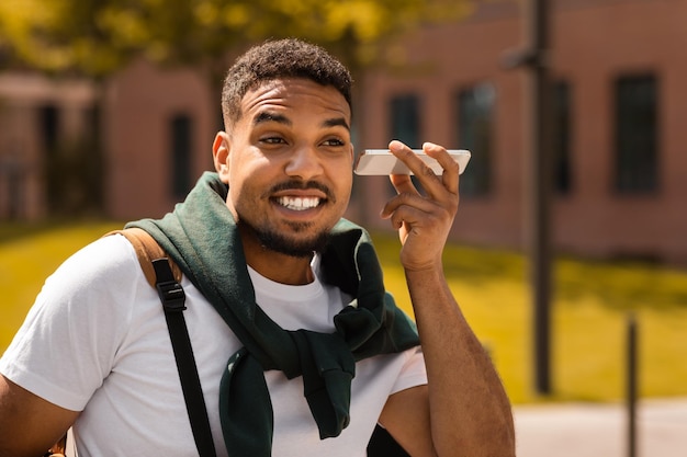 Young stylish african american man listening audio message on smartphone walking in park in the city