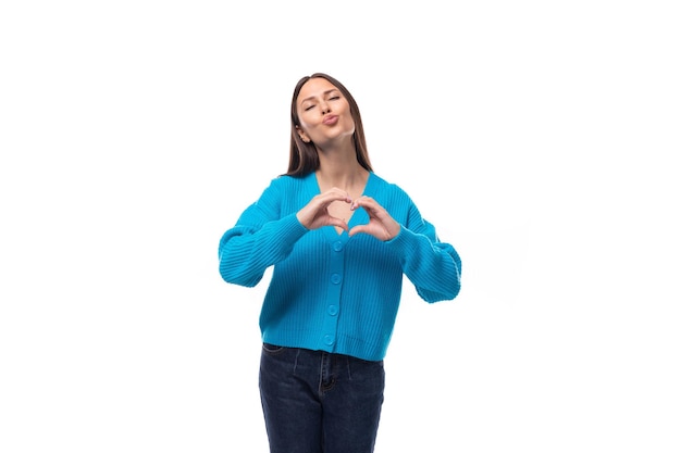 Foto giovane brunetta alla moda vestita con un maglione blu vneck mostra un cuore su uno sfondo bianco con