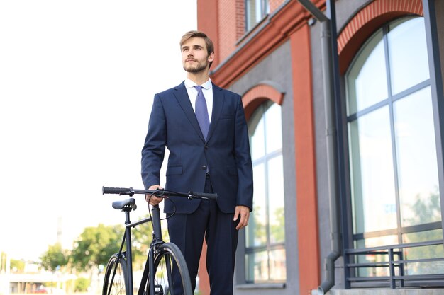 Young stylish business man dressed in suit walking with a bicycle on a city street.