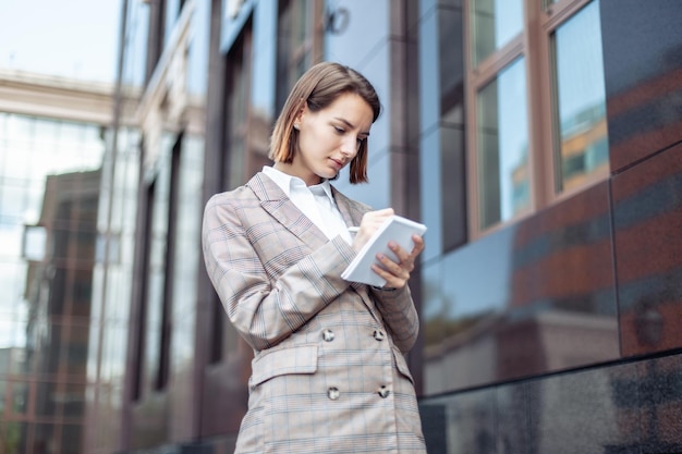 Young stylish business woman notes important information in a notebook against the background of a business building