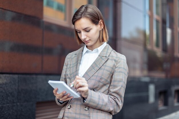 Young stylish business woman notes important information in a notebook against the background of a business building