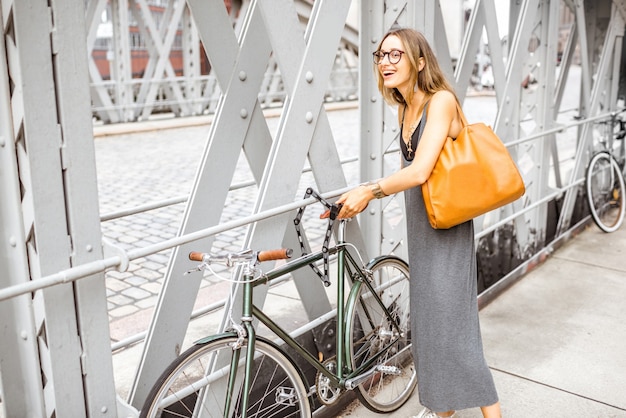 Young stylish business woman parking retro bicycle on the iron bridge