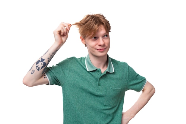 Young stylish cheerful european guy with red hair with a tattoo on his forearm wears a green tshirt