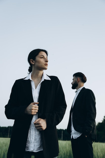 Young stylish couple of husband and wife dressed in classic suits on a photo shoot in the middle of a green field The concept of the relationship between a couple of people in love